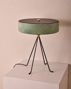 a green table lamp sitting on top of a white pedestal next to a pink wall