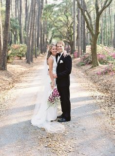 a bride and groom standing in the middle of a road surrounded by trees with pink flowers