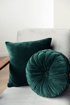 two green velvet pillows sitting on top of a white couch next to a wooden chair