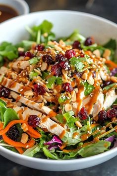 a salad with chicken and cranberries in a white bowl on top of a table