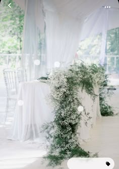 the table is covered with white linens and greenery