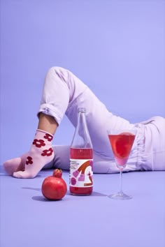 a woman laying on the floor next to a bottle of wine and a glass with an apple