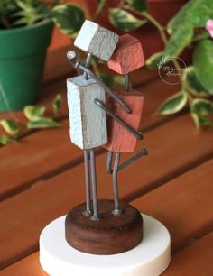 a small wooden sculpture on top of a table next to a potted plant with flowers in the background