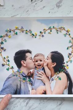 a man and woman holding a baby in front of a heart shaped photo