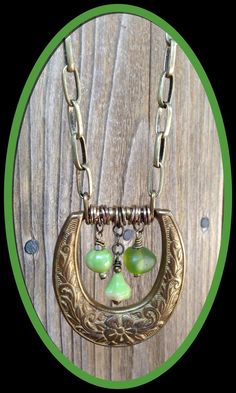 a gold necklace with green glass beads hanging from it's center circle on a wooden background