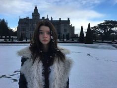 a woman standing in front of a large building with snow on it's ground