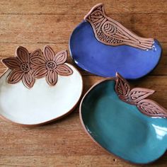 three plates with designs on them sitting on a wooden table next to another plate that has flowers in it