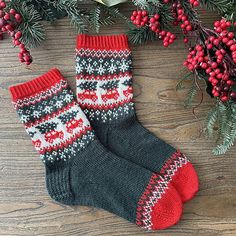 two knitted christmas socks sitting on top of a wooden table next to holly branches