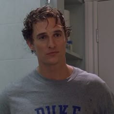 a man with curly hair standing in front of a bathroom mirror looking at the camera