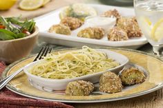 a plate full of spaghetti and meatballs next to a bowl of salad with lemon wedges