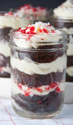 four desserts in glass jars with white frosting and red sprinkles