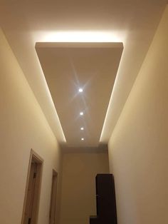 an empty hallway with some lights on the ceiling and stairs leading up to the door