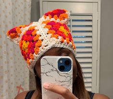 a woman taking a selfie with her cell phone wearing a crocheted hat