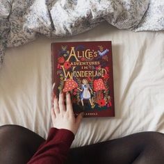 a person laying in bed reading a book about alice and the wonderful world of wonderland