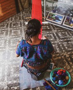 a woman sitting on the floor next to a bowl of yarn