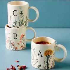 three coffee mugs with flowers and letters on them