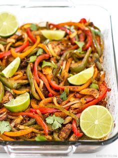 a glass casserole dish filled with chicken, peppers, and lime wedges