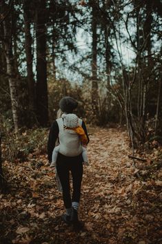 a woman walking through the woods carrying a baby