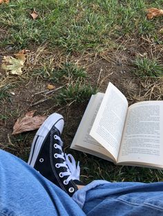 an open book sitting on the ground next to someone's legs and shoes with their feet crossed