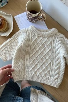 a person sitting at a table with a cup of coffee and a sweater on it