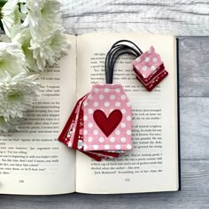 an open book with two pieces of fabric attached to it and flowers in the background