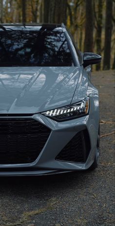 the front end of a gray car parked in a wooded area