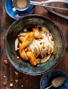 a bowl filled with ice cream and bananas on top of a wooden table next to spoons