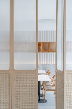 a room divider with white walls and wooden chairs around it in front of a dining table