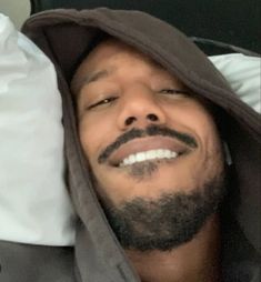 a man with a goatee smiles while laying on a bed in a hoodie