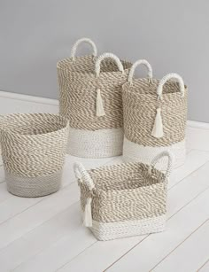 four woven baskets with tassels on the handles and sides, all in different sizes