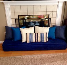 a blue couch sitting in front of a fireplace with two pillows on top of it