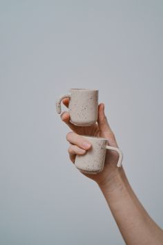 a hand holding two mugs in each other's hands, both with handles