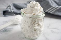 a glass jar filled with whipped cream on top of a marble counter next to a spoon