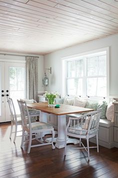 a dining room table with four chairs and a bench in front of two windows that look out onto the woods