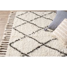 a white and black rug with fringes on the floor next to a blue pillow