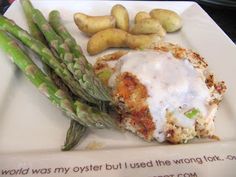 a white plate topped with asparagus and meat covered in gravy next to potatoes