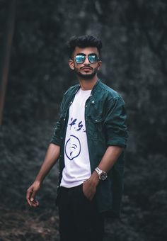 a man with sunglasses on standing in front of trees