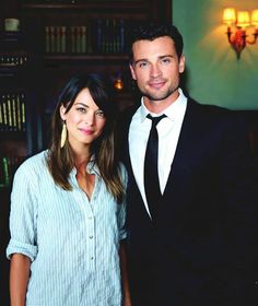 a man and woman standing next to each other in front of a book shelf filled with books