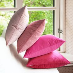 three pink and purple pillows sit on a window sill