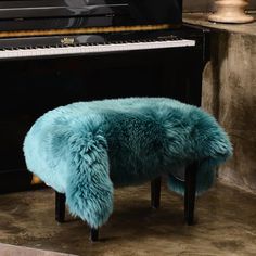 a blue stool sitting in front of a piano with a fur rug on top of it