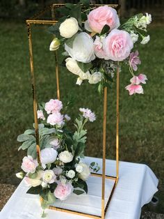 some pink and white flowers are on a gold stand with greenery in the background