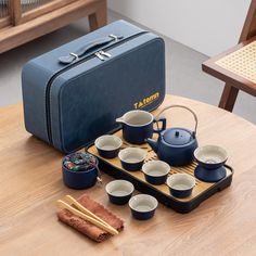 a tea set on a wooden table next to a blue suit case and chopsticks