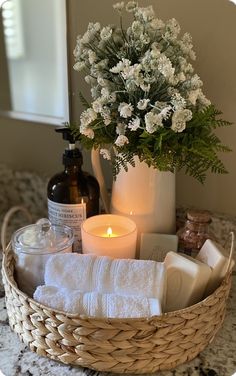 a basket filled with white towels next to a candle and some bottles on a counter