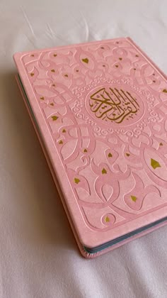 a pink book with gold foil on it sitting on a white tablecloth covered surface