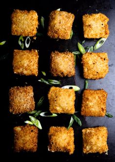 several square pieces of food on a black surface with green onions and olives next to them