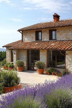 an old stone house with potted plants and lavender in the foreground on a sunny day