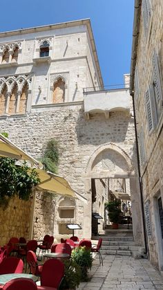 an alley way with tables and chairs lined up against the wall, in front of a stone building