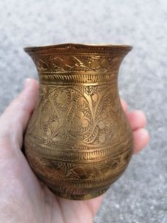 a hand holding a gold colored vase in it's left hand on the ground