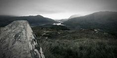 a view of mountains and water from the top of a hill with grass on both sides