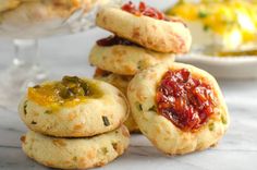 several cookies with jam on them sitting next to a glass dish full of other pastries